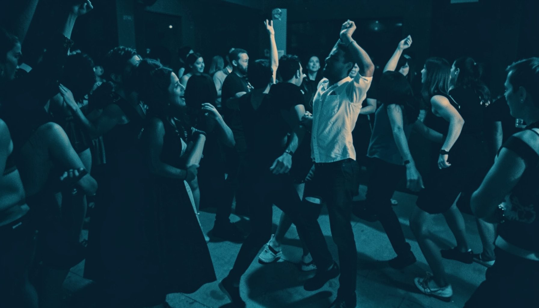 Duotone image of dancers moving in a lively social setting, amber highlights against deep blue shadows