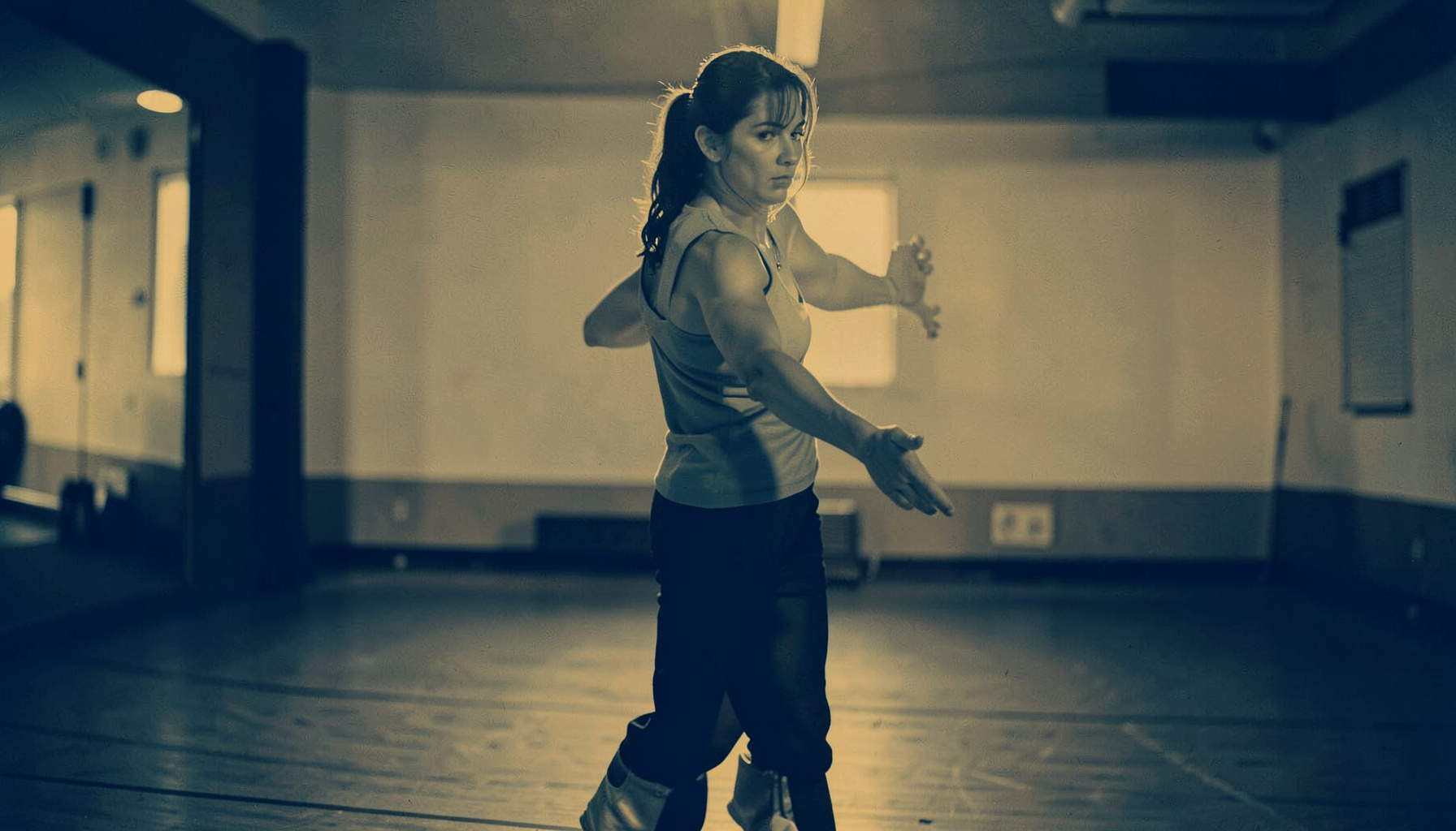 Duotone portrait-style image of a dance instructor in a studio, warm amber and navy tones