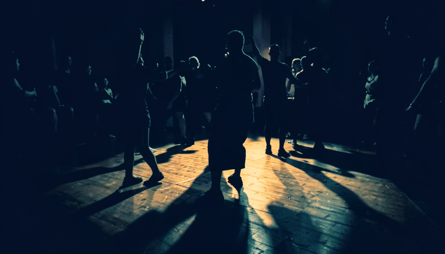 Duotone photograph of a dance floor with warm amber light cutting through deep navy shadows, evoking the energy of Latin dance