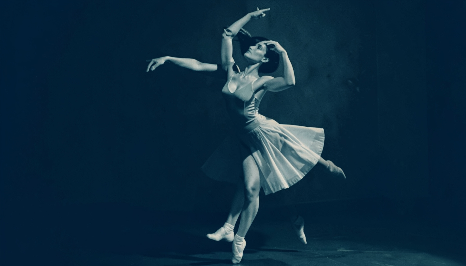 Duotone of a ballet dancer in a graceful pose, soft amber light and deep navy shadows